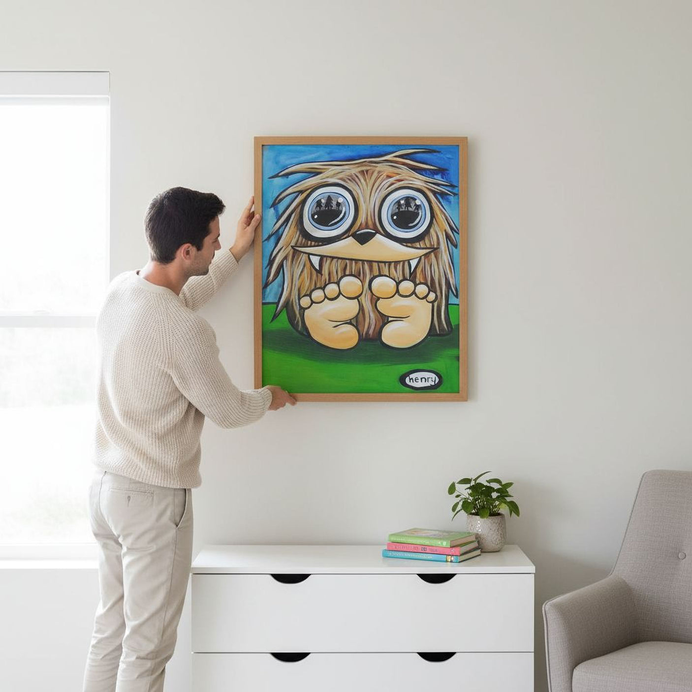 A man is hanging a large, colorful painting of a cartoon character on a wall in a room with a white dresser and a plant.