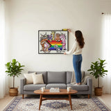A man is standing on a stool and hanging a colorful, abstract painting on a wall in a room with a potted plant and a white table.
